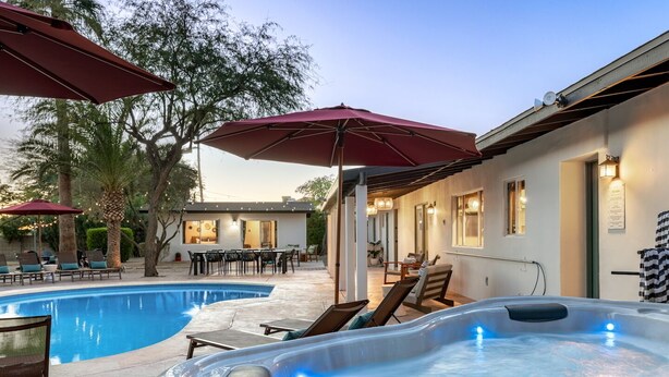 Una piscina, un jacuzzi, mobiliario exterior y un edificio con ventanas y luces.