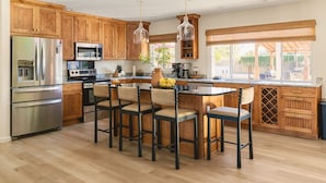 Una cocina con gabinetes de madera, electrodomésticos de acero inoxidable, una isla central con taburetes altos e iluminación colgante.