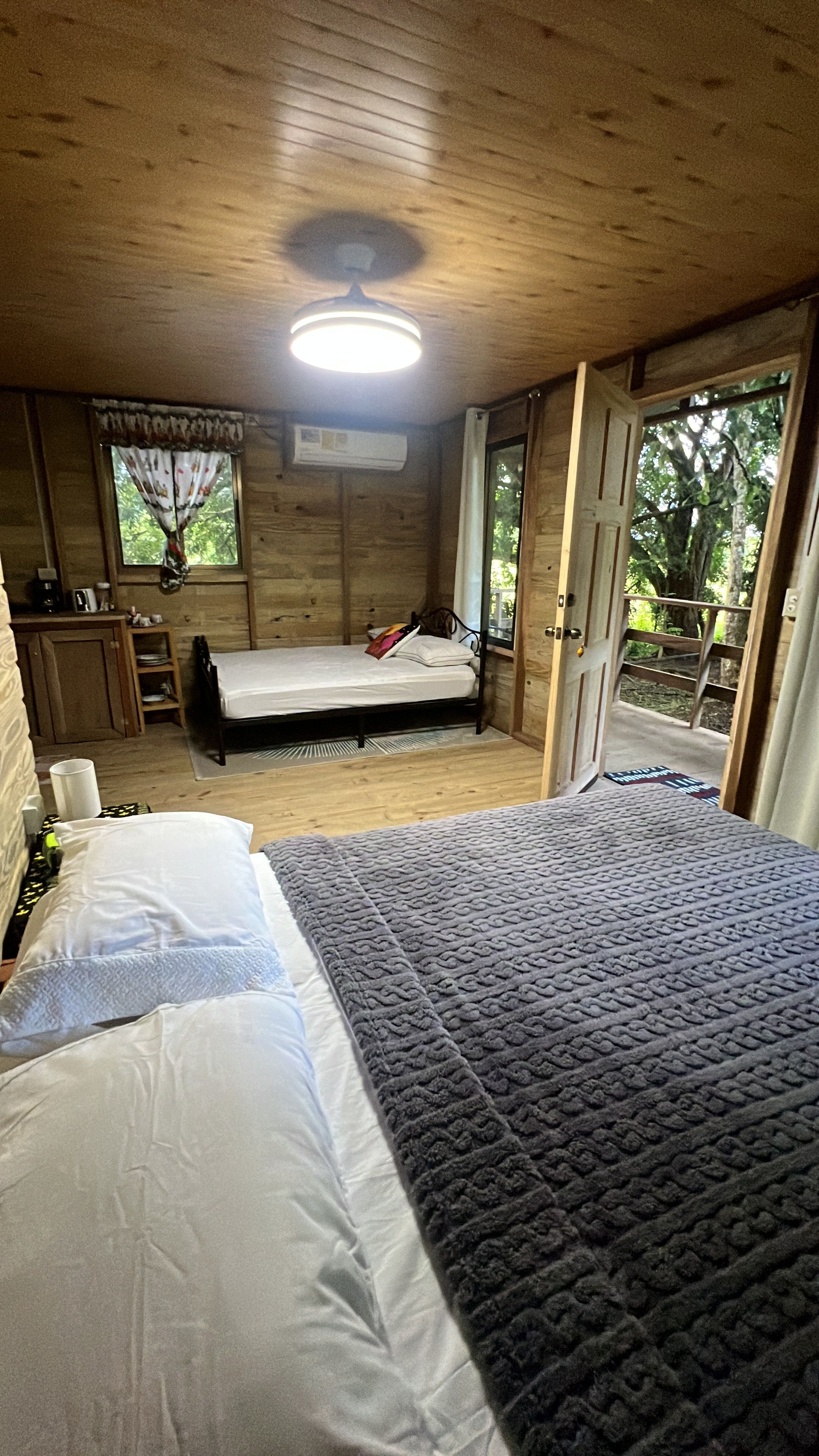 A wooden cabin bedroom with a bed, a desk, and a window.