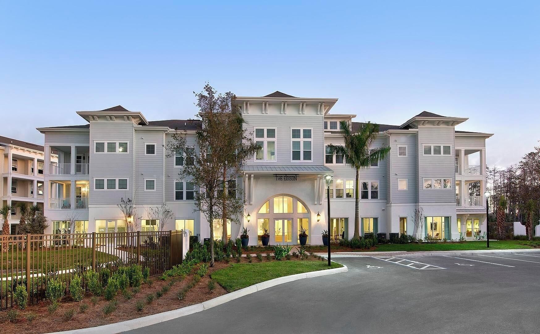 A multi-story hotel with a central entrance, balconies, and a landscaped front yard.