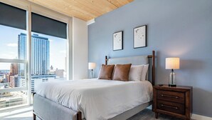 Une chambre avec un grand lit, deux tables de chevet, une vue sur la ville et un mur bleu.