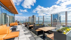 Une terrasse sur le toit avec des sièges extérieurs, une vue sur les gratte-ciel de la ville et un plan d’eau.