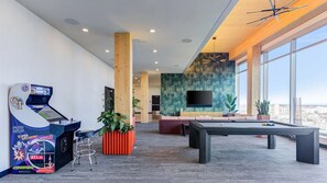 A modern lounge with a pool table, a gaming console, and a large window offering a city view. - Landing | Incredible 1BD, Gym, Pool (Milwaukee)