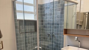 A bathroom with a glass-enclosed shower, a white toilet, a sink with a black countertop, and a mirror above the sink. - New Studio • Sea view • 2 minutes with your feet in the sand (Rio de Janeiro)