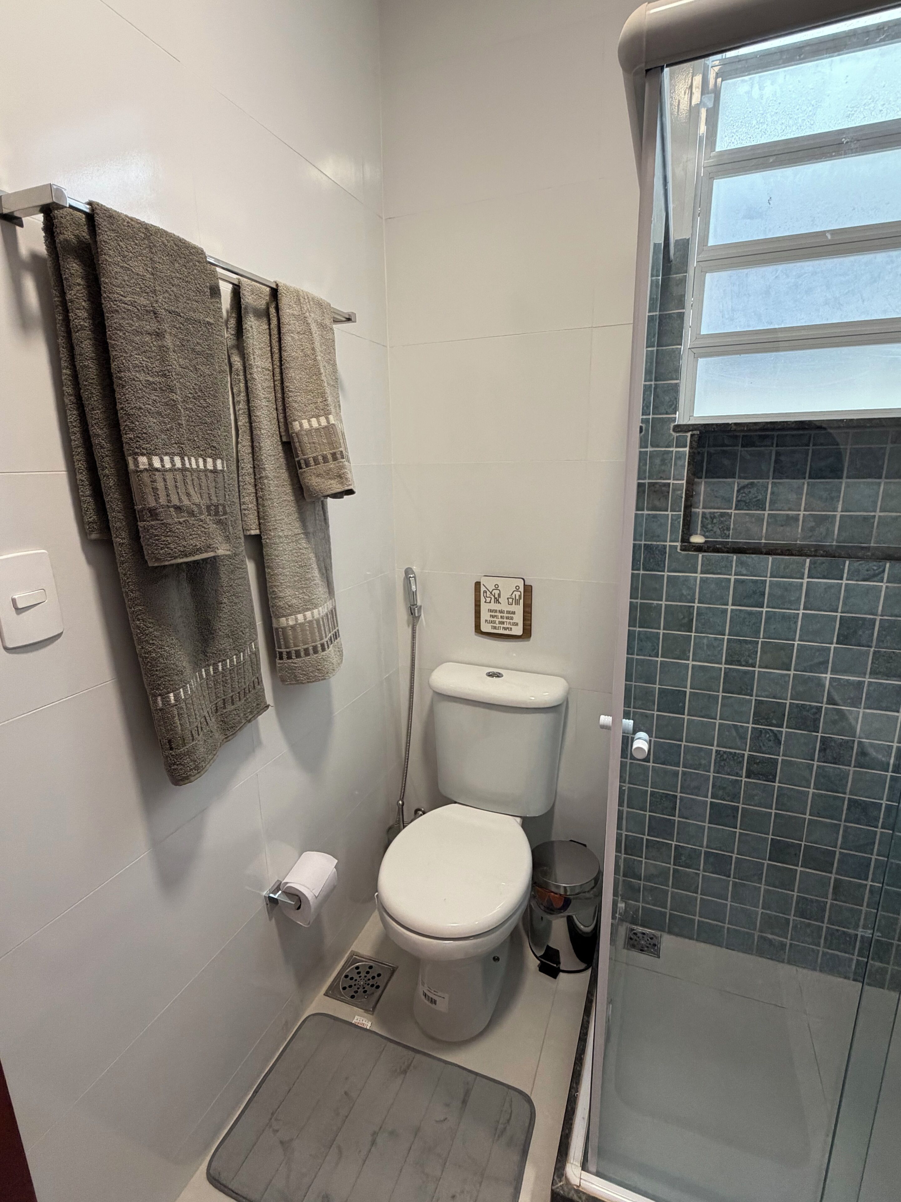 A bathroom with a toilet, shower, and a towel rack with multiple towels.
