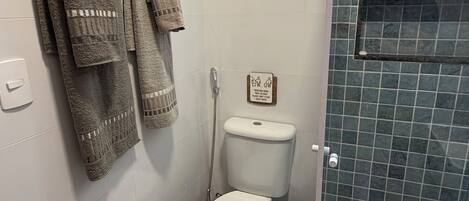 A bathroom with a toilet, shower, and a towel rack with multiple towels.