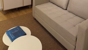 A living room with a sofa, a small table, a bookshelf, a red appliance, and a wall-mounted picture. - New Studio • Sea view • 2 minutes with your feet in the sand (Rio de Janeiro)