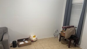 Ett rum med en grå soffa, en liten papperskorg, en kartong, en plastpåse och en stol med en kudde.
