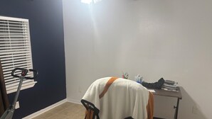 Een kamer met een hometrainer, een fauteuil, een bureau met een computer en een stopcontact.