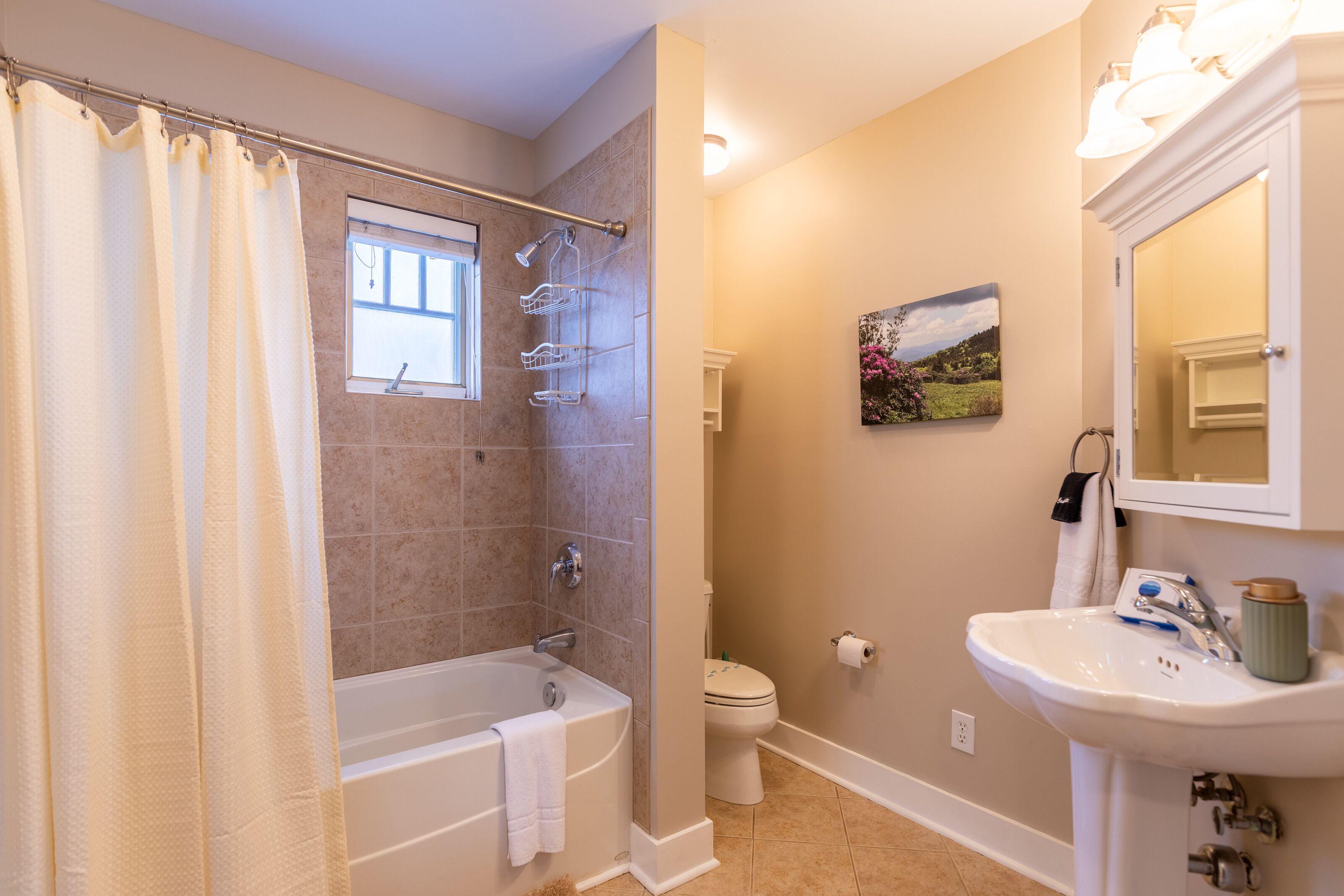 A bathroom with a bathtub, toilet, and sink, featuring beige walls and a window.