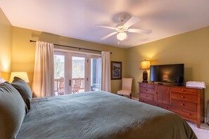 Een slaapkamer met een bed, een televisie, een dressoir, een stoel en een balkon.