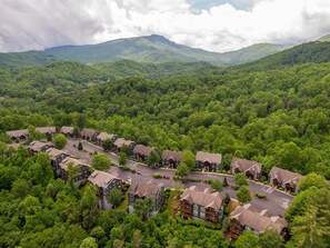 A resort with multiple buildings, a central road, and lush green forested hills in the background. - Gateway to Grandfather | Community Pools, Mountain View, Fitness Rooms, and More (Boone)