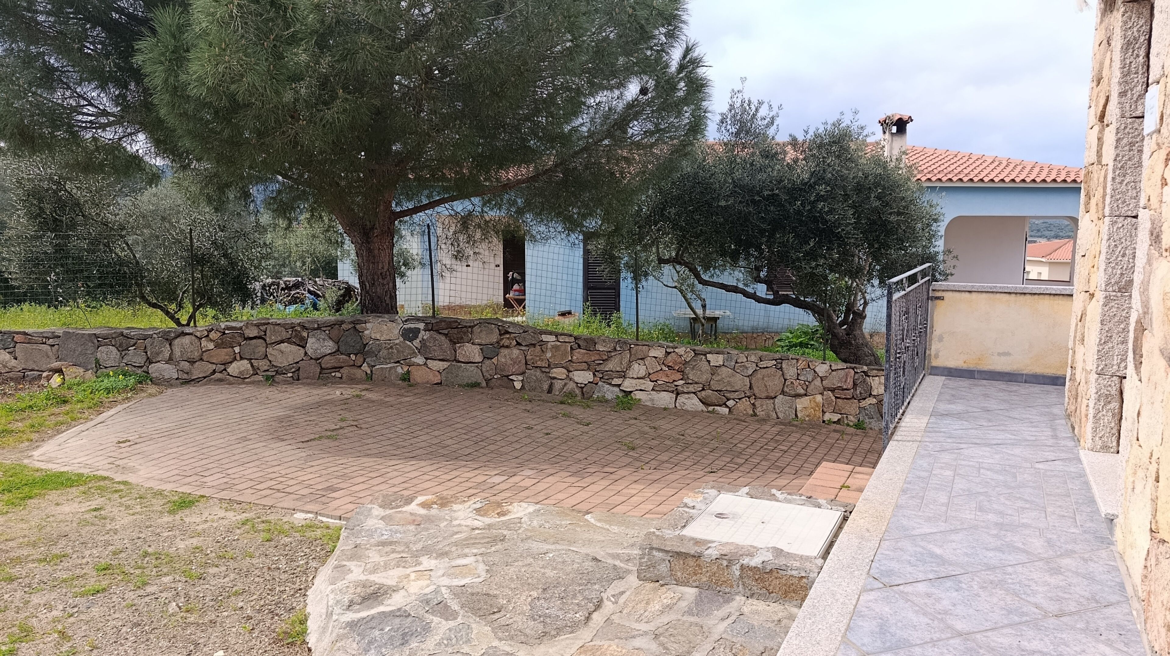 Une terrasse en pierre avec un mur en pierre, un arbre et un bâtiment avec un toit en tuiles en arrière-plan.