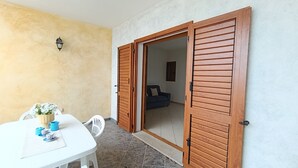 Une pièce avec une table blanche, des tasses bleues, une plante en pot et une porte en bois donnant sur une autre pièce.