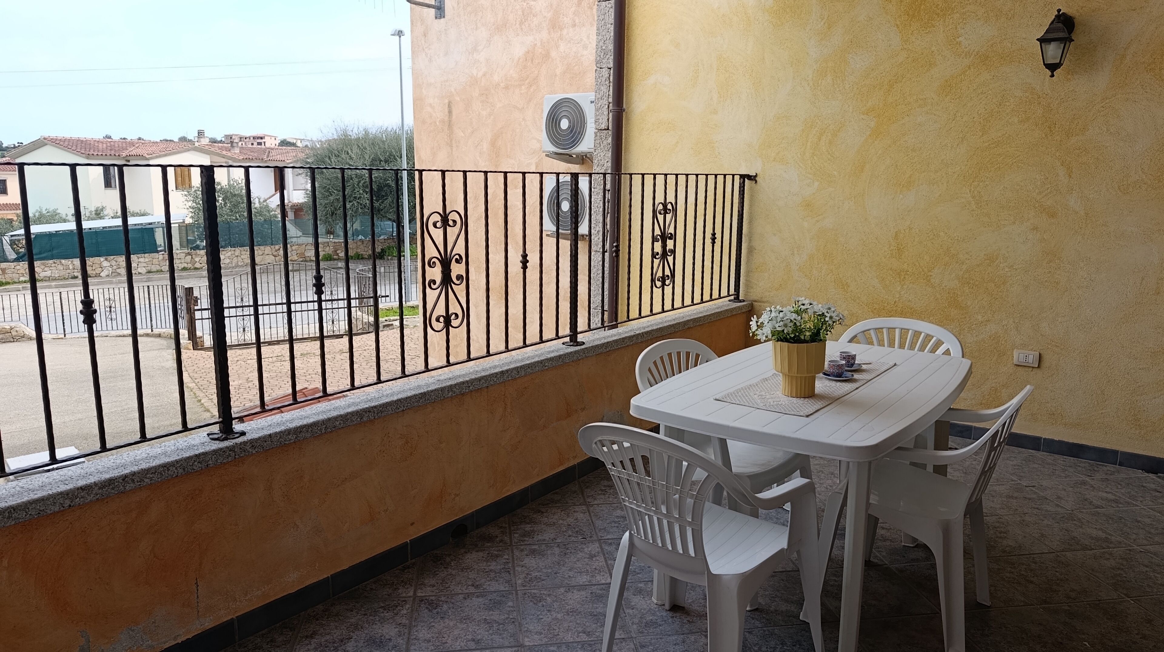 Ein Balkon mit einem weißen Tisch und Stühlen, einer Blumenvase und Blick auf die Straße.