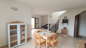 Un coin repas avec une table dressée pour quatre personnes, un buffet bleu clair aux portes vitrées, un escalier et un téléviseur fixé au mur.
