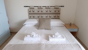 Un lit bien fait, avec du linge de lit blanc, une tête de lit décorative et une table de chevet sur laquelle est posé un vase.