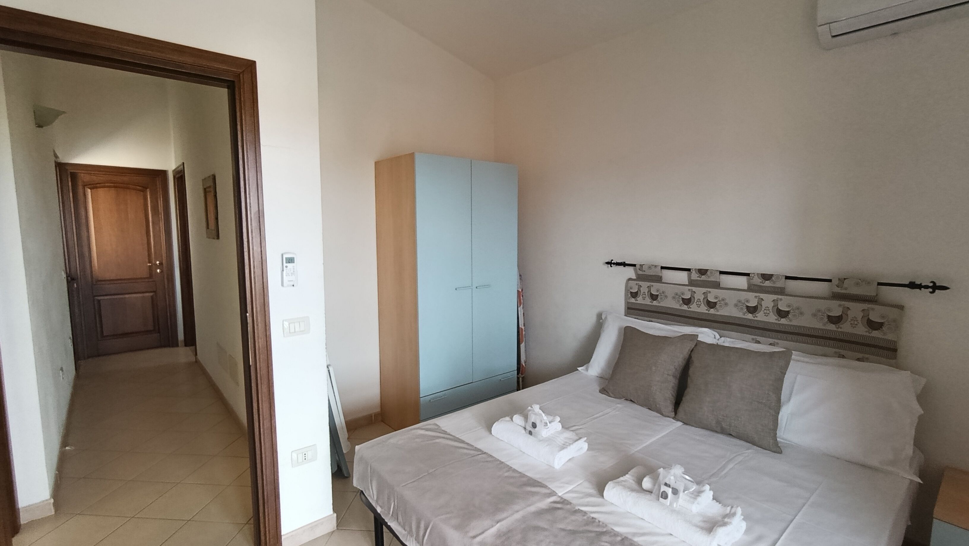 A bedroom with a bed, a wardrobe, a door, and a hallway.