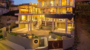 Un hotel moderno de varios pisos con fachada curva, asientos al aire libre y una escalera que lleva a los niveles superiores.