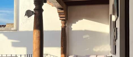 A balcony with a wooden pergola, a seating area with cushions, a small table, and a potted plant.