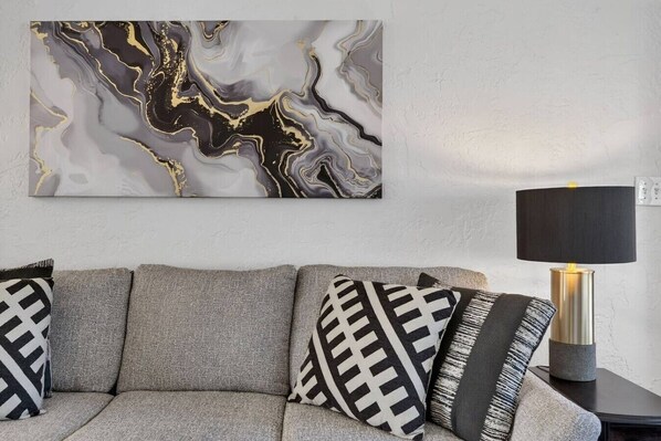 A modern living room with a gray sofa, patterned cushions, a marble artwork, and a lamp on a side table.