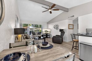 A modern living room with a dining area, a kitchen, and a ceiling fan.