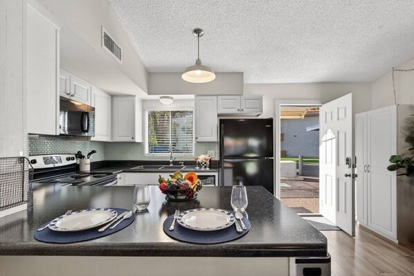 A modern kitchen with white cabinets, a black refrigerator, and a dining area with a glass table set for two.