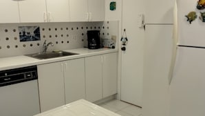 Keittiössä on valkoiset kaapit, astianpesukone, kahvinkeitin ja jääkaappi, jonka oveen on kiinnitetty magneetteja.