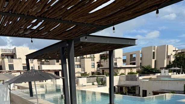 Un espace piscine aménagé avec des chaises longues, des parasols et une structure en forme de pergola.