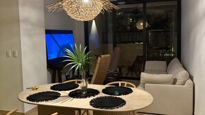 Un coin repas avec une table ronde, des chaises, un luminaire suspendu et un téléviseur en arrière-plan.