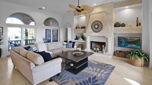 A living room with a sofa, coffee table, fireplace, television, and decorative items. - Waterfront Neo Mediterranean Home On Casey Key - Tidewater Manor (Nokomis)