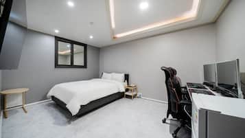 A modern bedroom with a bed, bedside table, and a desk with a computer.