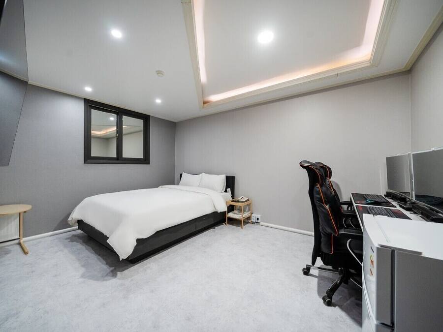 A modern bedroom with a bed, bedside table, and a desk with a computer.