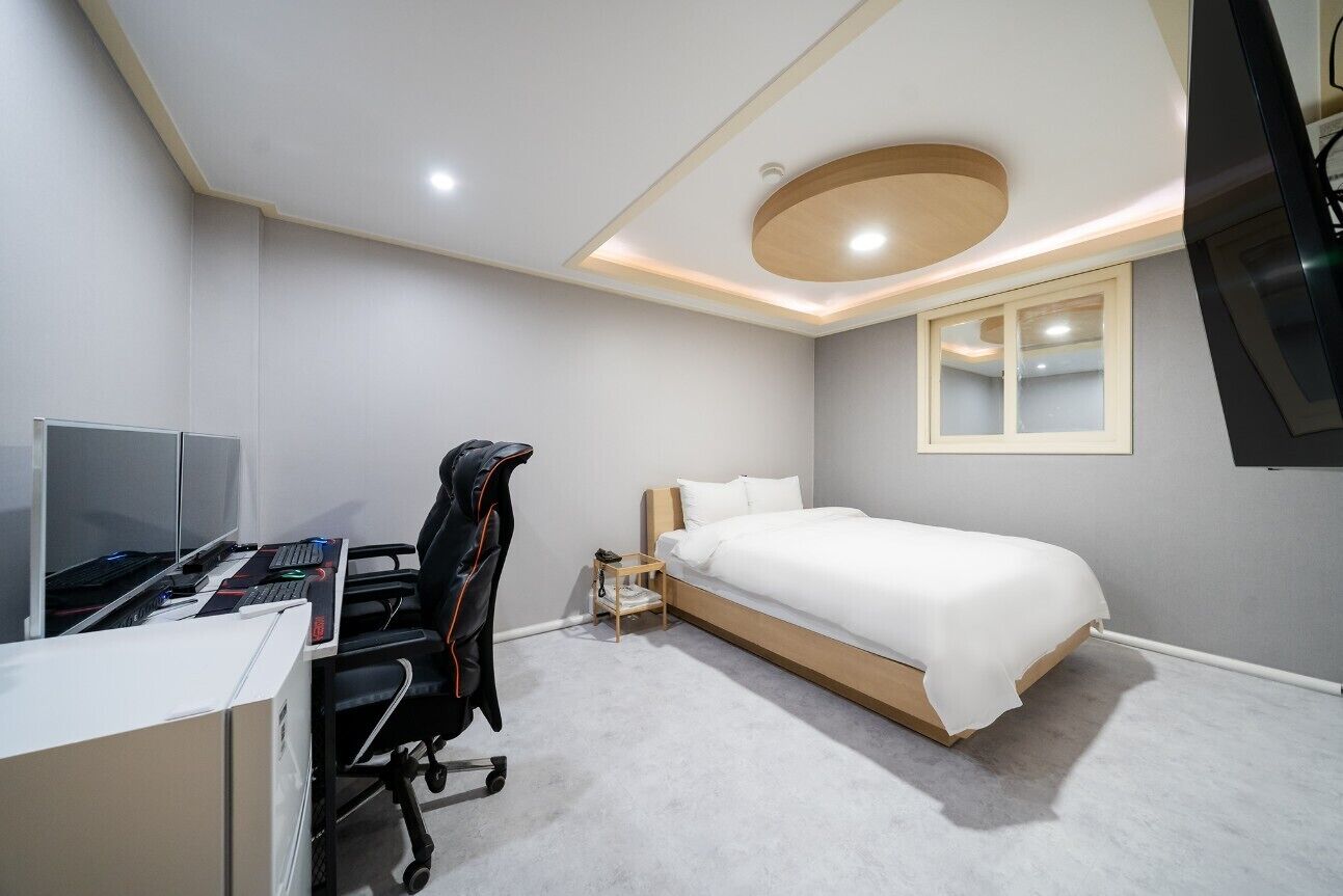A modern bedroom with a bed, desk, and chair, a TV, and a small table.