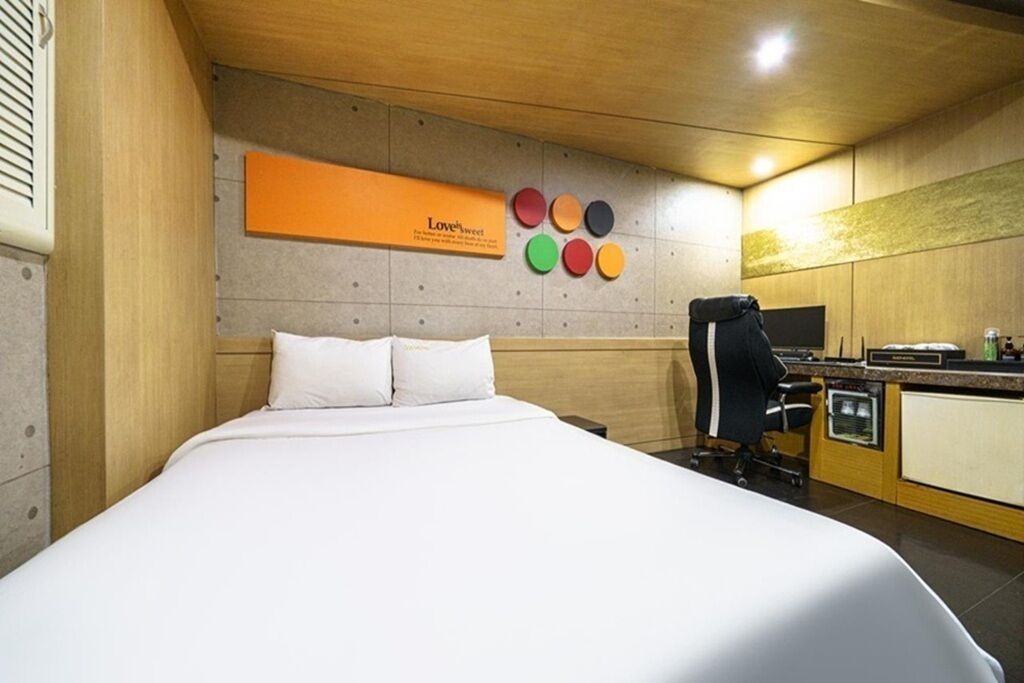 A hotel room with a bed, a desk, a chair, and a wall-mounted TV.