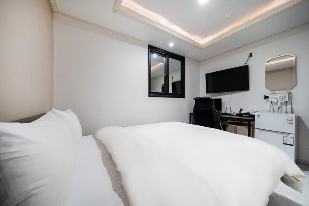 A hotel room with a bed, a desk, a chair, a television, and a mirror.
