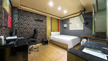 A hotel room with a bed, desk, chair, and a bathroom with a sink and mirror.