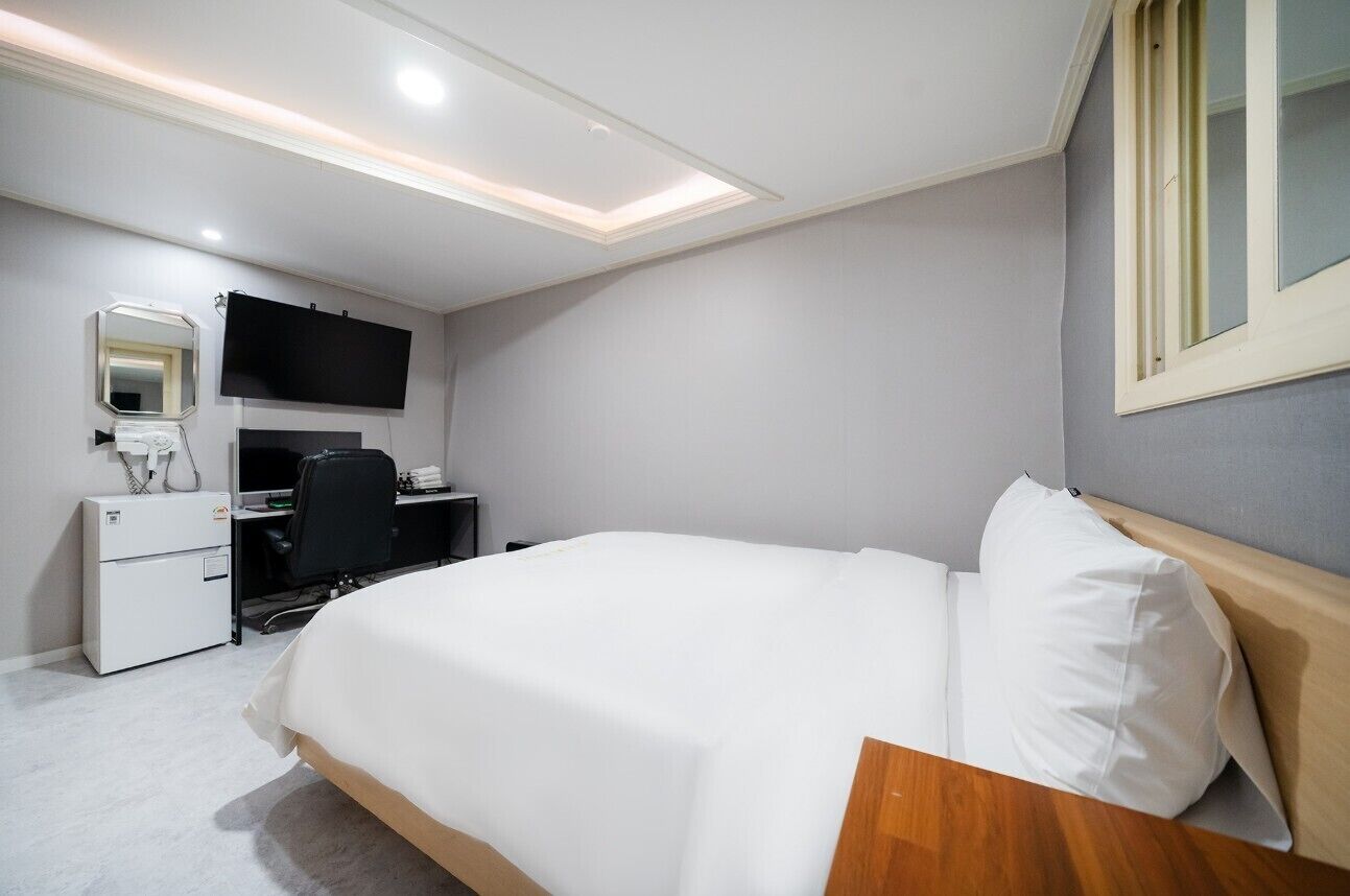 Ein Hotelzimmer mit Bett, Schreibtisch, Stuhl, Flachbildfernseher, Spiegel und Fenster.