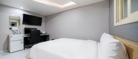 Ein Hotelzimmer mit Bett, Schreibtisch, Stuhl, Flachbildfernseher, Spiegel und Fenster.