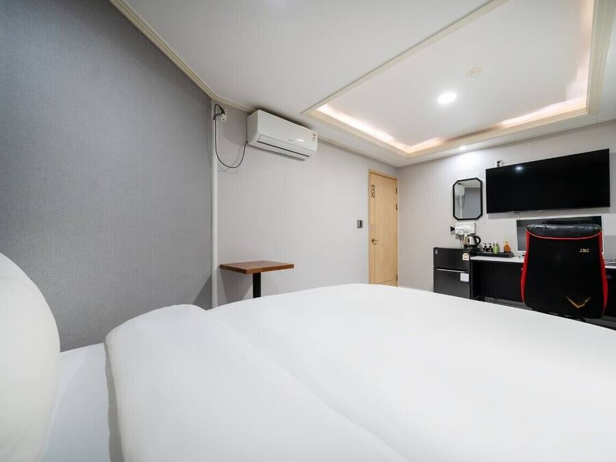 A hotel room with a bed, a desk, a chair, a TV, and an air conditioning unit.