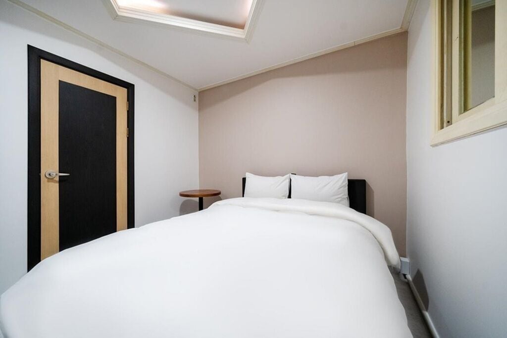 A bedroom with a bed, a round side table, a door, and a window.