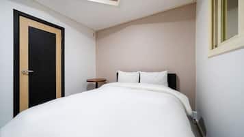 A bedroom with a bed, a round side table, a door, and a window.