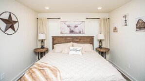 Slaapkamer met een groot bed, twee nachtkastjes met lampen, een houten hoofdbord, een sterdecoratie en een kunstwerk aan de muur.
