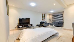 A modern hotel room with a large bed, a flat-screen TV, a sofa, and a dining table. - 1 King, 4 Double bed, 2 Sofa bed, 2 Parking, 12ppl (Monterrey)