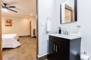 Een hotelkamer met een bed, een badkamer met wastafel en spiegel, en een plafondventilator.
