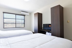 Een hotelkamer met twee bedden, een televisie op een houten standaard en een airconditioning aan de muur.