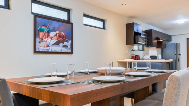 A dining area with a long wooden table set for four, a painting on the wall, and a kitchen in the background. - 1 King, 4 Double bed, 2 Sofa bed, 2 Parking, 12ppl (Monterrey)