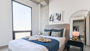 Un dormitorio moderno con una cama grande, una mesita de noche con lámpara y vistas al exterior.
