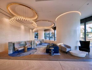 A modern lobby with a central seating area, a large column, and a chandelier. - CBD 2BR Getaway | River Views, Pool & Gym  Share  Save (Brisbane)