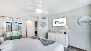 Une chambre d’hôtel avec un lit, un ventilateur de plafond, une télévision, une horloge et une vue sur la ville.
